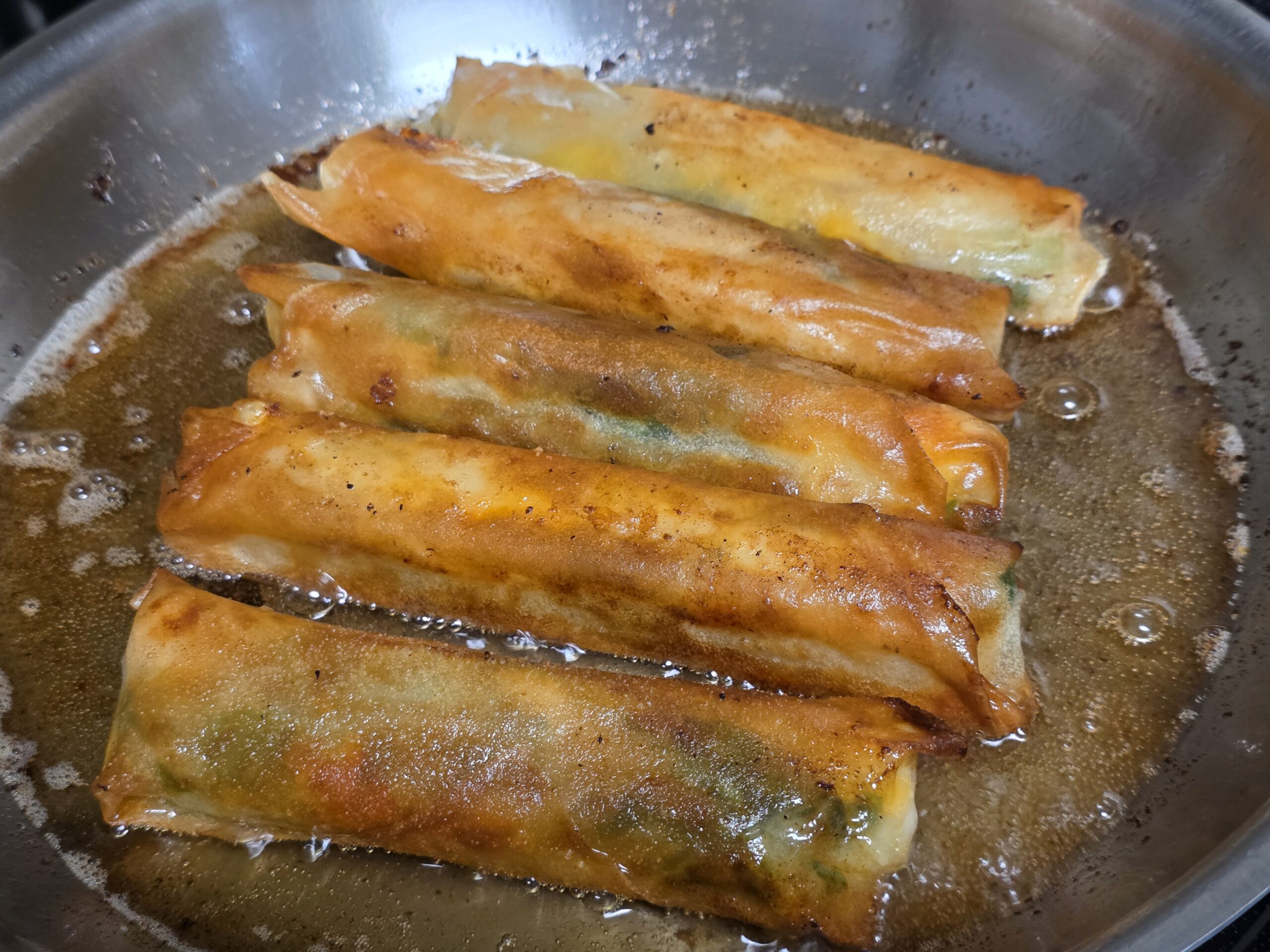 Handmade spring rolls cooking in a pan.